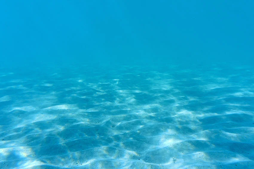 View of the sandy ocean bottom, with sunlight striking through the exceptionally clear water.
