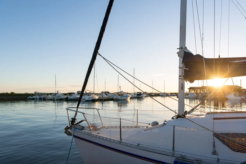 View of a small fishing boat marina in Venice, Louisiana, with several boats docked along quiet waters and a warm sunset glowing in the background.