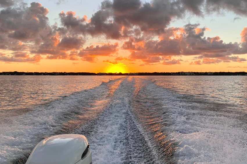Action shot of a boat leaves a broad wake across coastal water at sunset while traveling toward the open Gulf for a fishing trip.