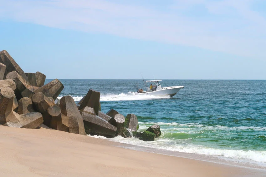 View from the shore of a fishing charter speeding near the Alabama Point Jetties with waves trailing behind.