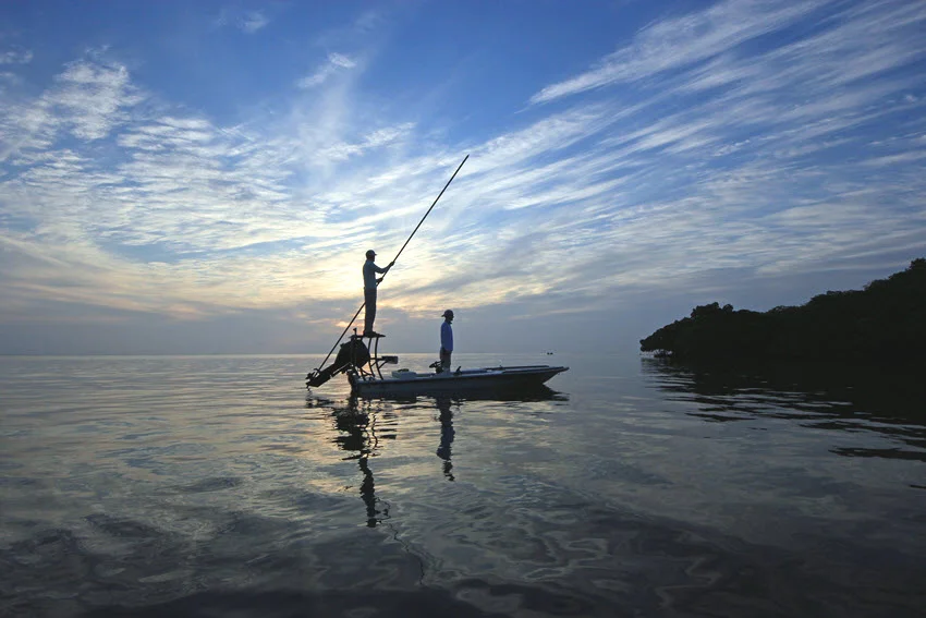 View of anglers on a small boat searching for the perfect spot for sight fishing during sunset.