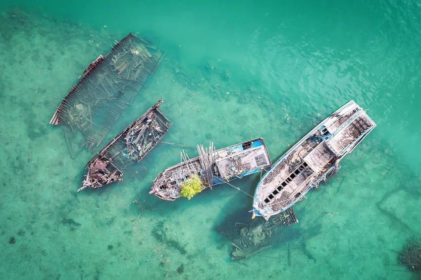 Aerial view of a few old fishing boats drifting on the calm blue-green shallow waters with sandy patches visible beneath the surface.