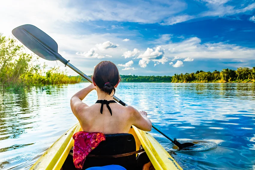 Kayaker paddling across the Amazon River in Brazil, part of the Peacock Bass species' native tropical freshwater range.