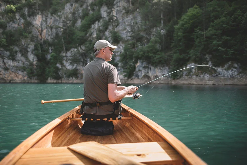 Angler casting from a wooden canoe on a sheltered lake, illustrating small-boat access for Peacock Bass fishing.