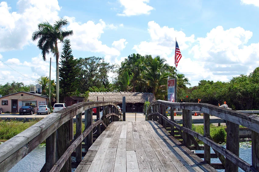 Wooden footbridge leading toward an Everglades airboat area near freshwater habitat used for fishing across South Florida.