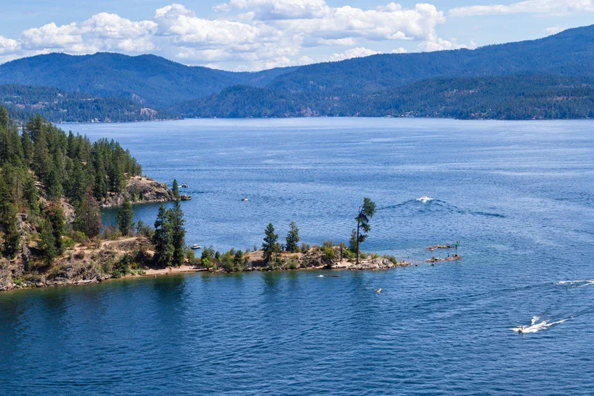 Wide view of Lake Cascade, Idaho, with forested mountain slopes, blue water, and boats crossing a productive Perch fishing destination.