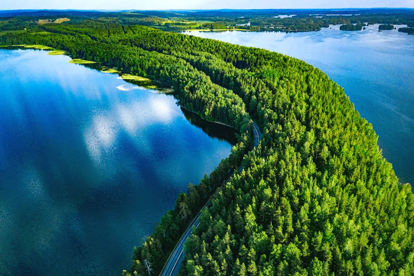 Aerial view of Lake Lestijärvi, Finland, showing a forested peninsula, shoreline road, and expansive blue water during summer.