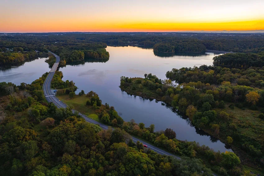Aerial view of Seneca Lake, New York, at sunrise, with a shoreline road, forested banks, and calm water surrounding small islands.