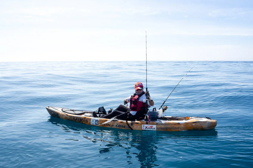 Angler in a kayak with two fishing rods, gliding through the open sea.