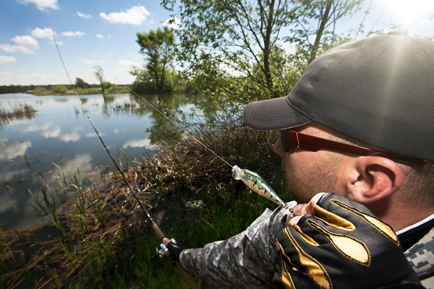 Close view of an angler wearing sunglasses and a cap while fishing in a river.
