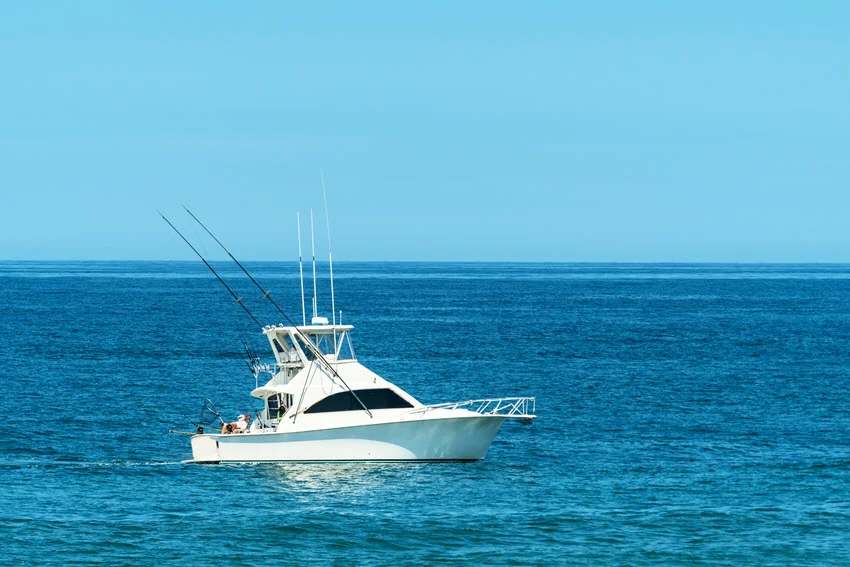 Distant view of a trolling boat gliding across the open ocean, with anglers and fishing equipment on board.