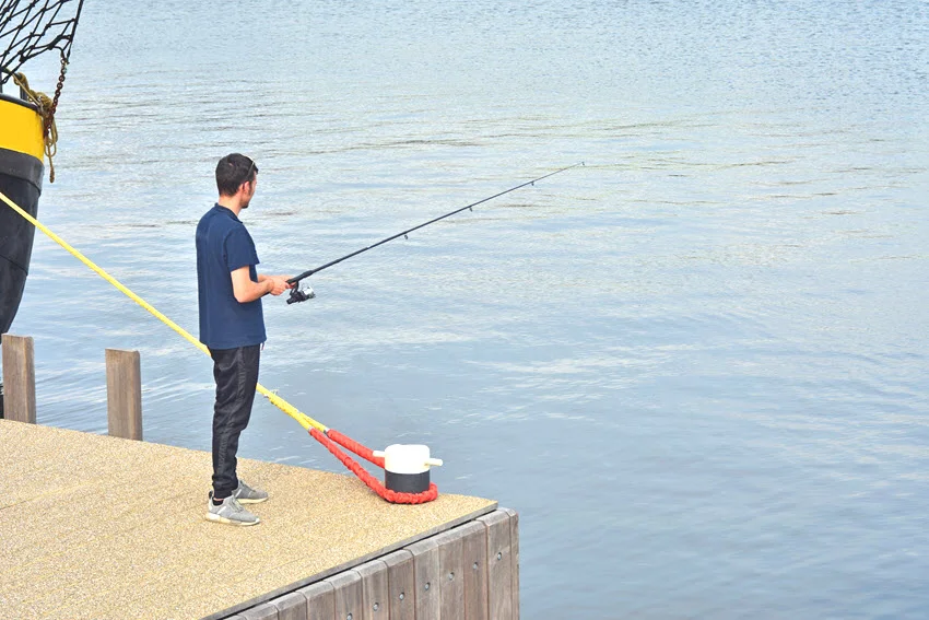 A man fishing from a stone pier, holding a fishing rod as he reels in a catch.
