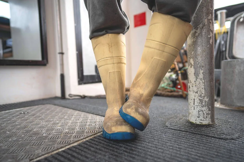 Angler dressed in gumboots and waterproof clothes, standing ready for a fishing trip. 