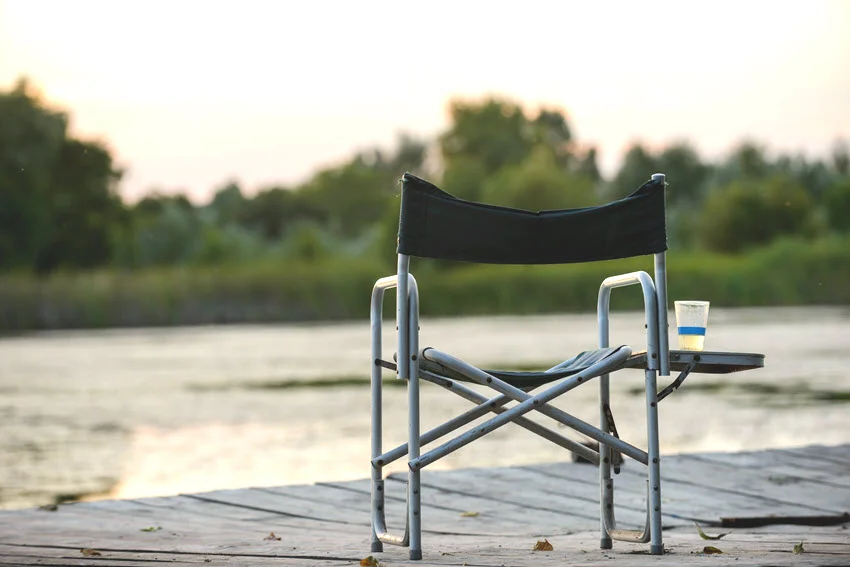 A folding chair placed on a pier at sunset, overlooking calm waters. A peaceful scene perfect for relaxation or fishing, with warm hues illuminating the horizon.