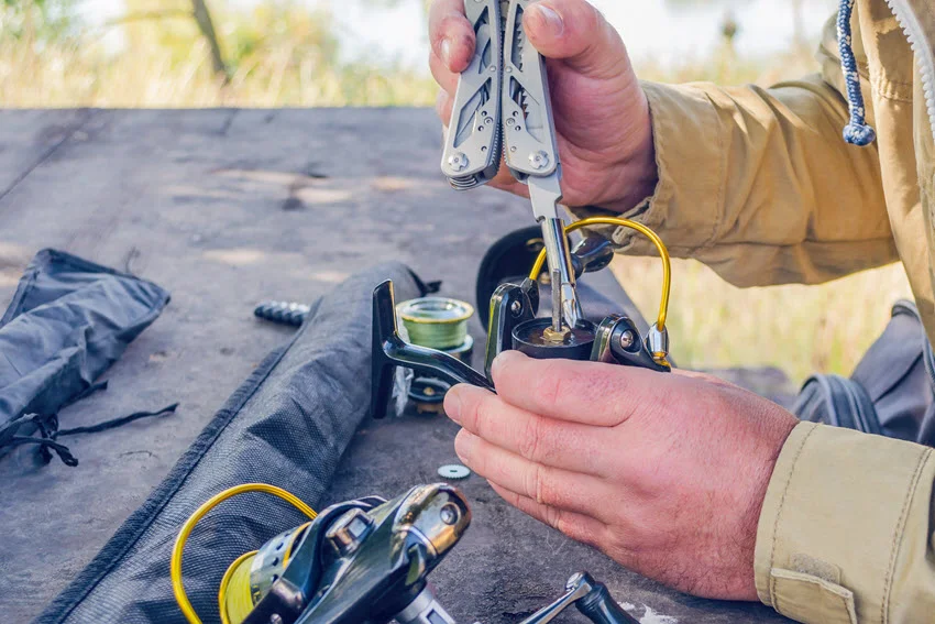 Close view of a man's hands repairing a fishing reel using improvised tools, with attention to detail on the delicate work.