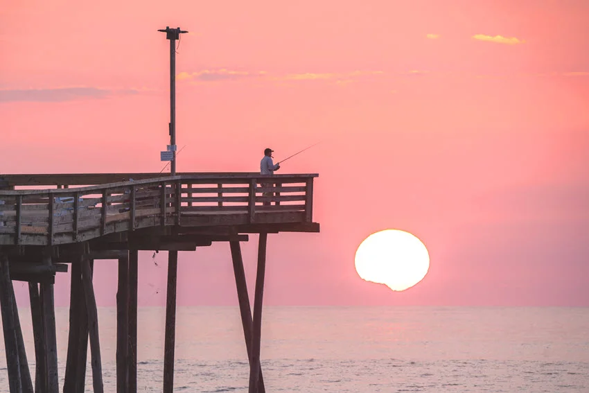 Sunrise at Virginia Beach, with a view of the fishing pier. A serene coastal scene highlighting the golden hues of the morning sky and the iconic pier.