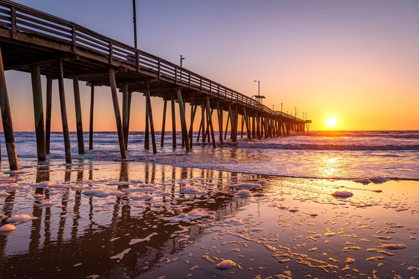 A view from the shore of the venerable wooden fishing pier in Virginia Beach, captured at sunrise with warm golden hues illuminating the scene.