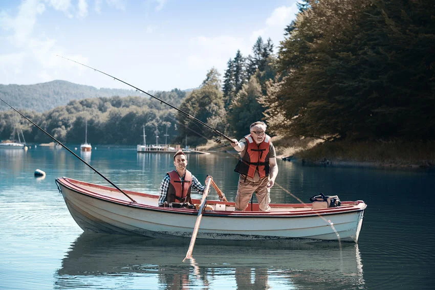 Two men on a traditional wooden fishing boat hold rods and perform pith fishing on a lake.