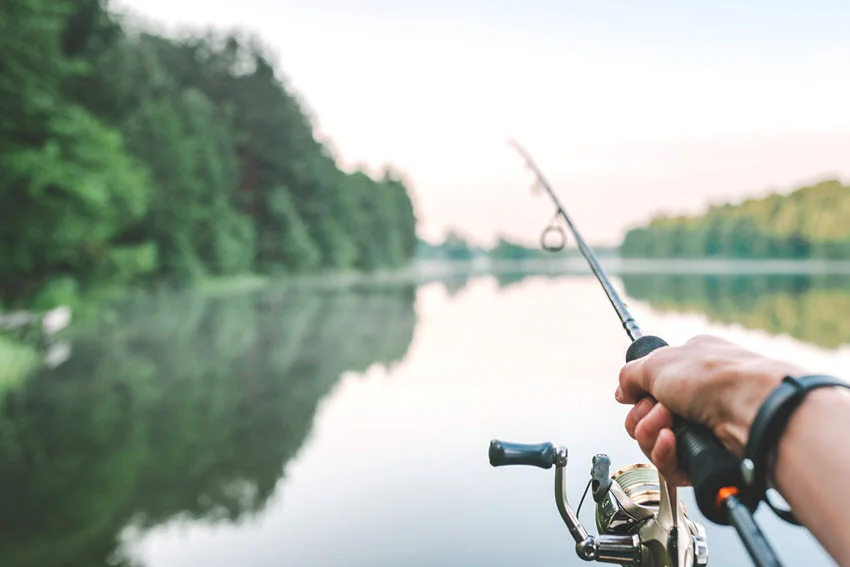 A view from the angler's perspective of a spinning rod, with a blurry river in the background.