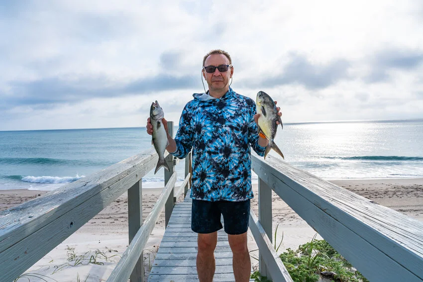 Angler standing on a beach access walkway along Florida's Atlantic Coast while holding two freshly caught Pompano after a successful surf fishing trip.
