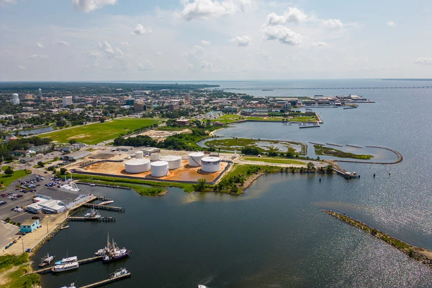 Boats, docks, and storage tanks line Pensacola's waterfront in Florida, with downtown buildings and the broad bay visible from above.