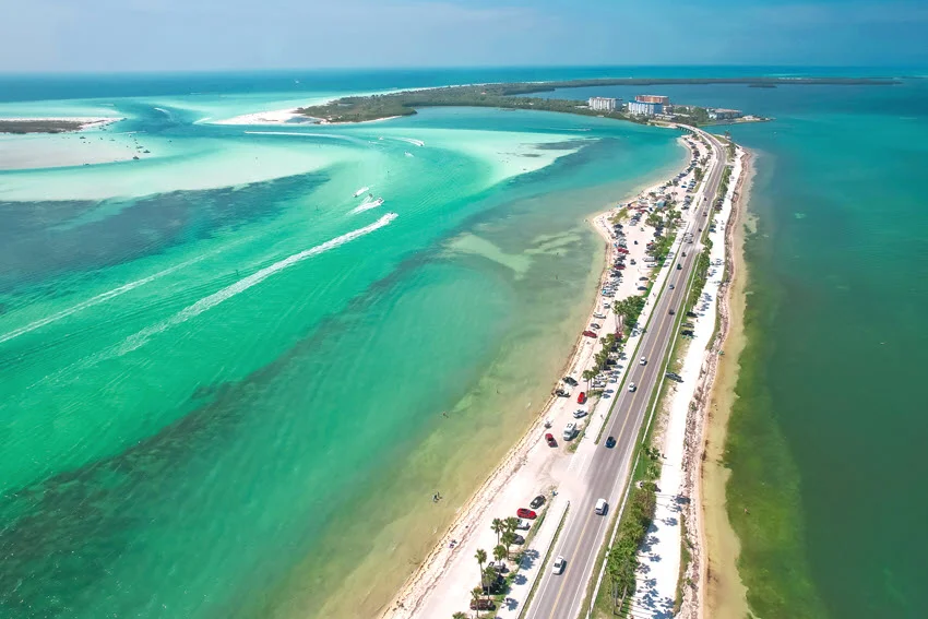 Aerial panoramic view of Honeymoon and Caladesi Island State Park in Florida, showcasing turquoise Gulf of Mexico water, sandy beaches, lush tropical nature, and the Dunedin Causeway on a bright summer day.
