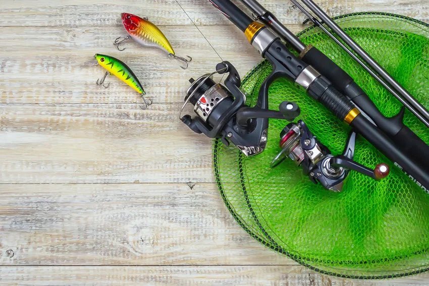 Fishing tackle with many colorful baits and a fishing rod placed on a wooden pier, ready for use.