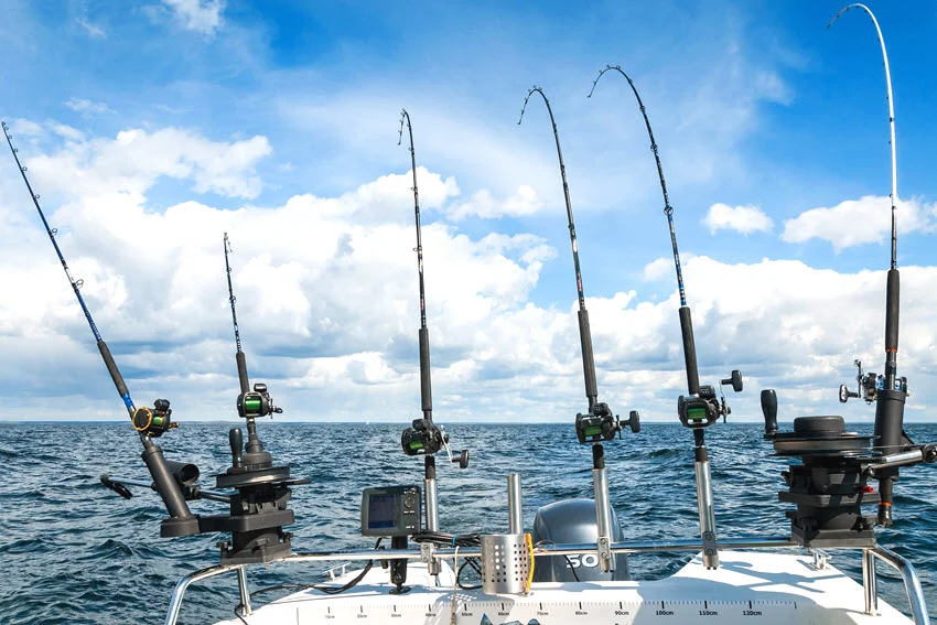 Multiple trolling rods set up on the back of a boat with reels and downriggers, ready for offshore fishing under a partly cloudy sky.