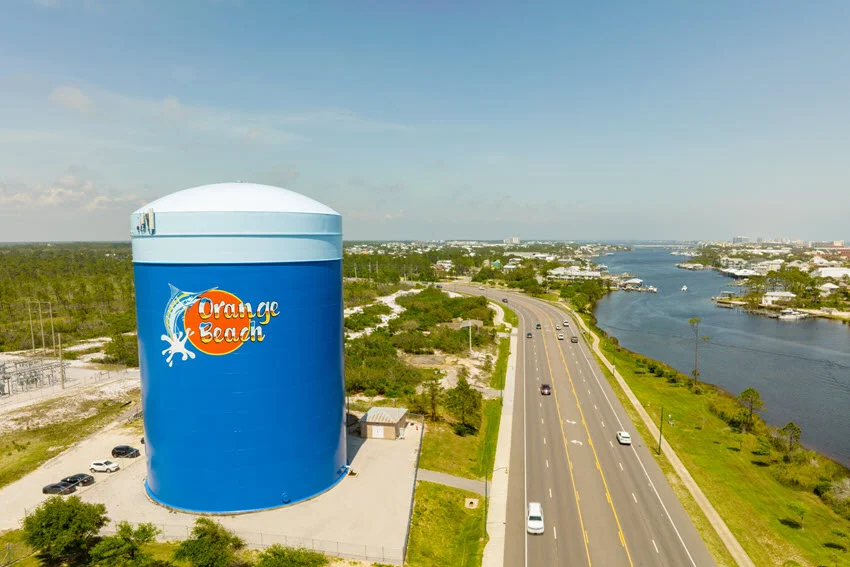 Aerial view of the large blue water tower with Orange Beach logo beside a coastal highway in Orange Beach, Alabama.