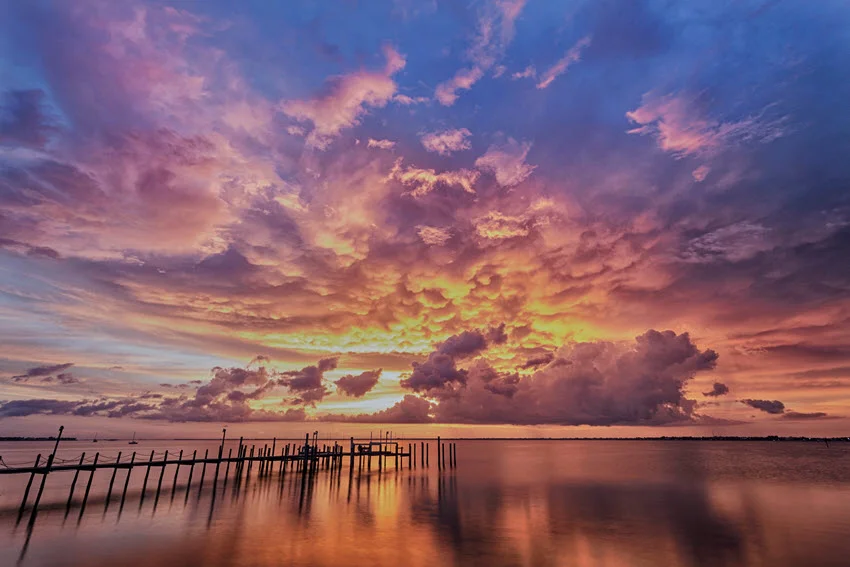 Wide scenic view of Charlotte Harbor, Florida at sunset with calm water, shoreline silhouettes, and dramatic clouds glowing over the bay.