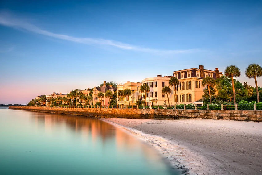 Waterfront view near Charleston, South Carolina, with calm harbor water, colorful homes, and a sandy shoreline under a bright sky.