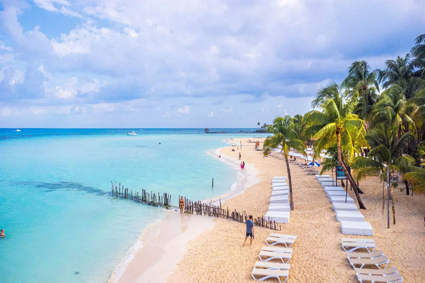 Beach view of Playa Norte on Isla Mujeres, Mexico, with white sand, palm trees, and clear shallow water near shore.