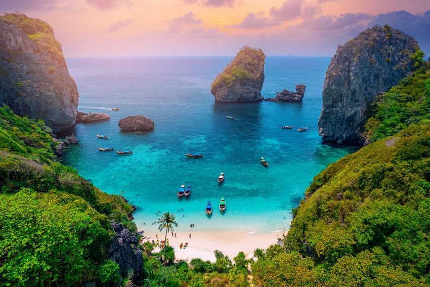 Lagoon view at Nui Beach in Krabi, Thailand, with emerald water, limestone cliffs, and boats anchored near the shore.