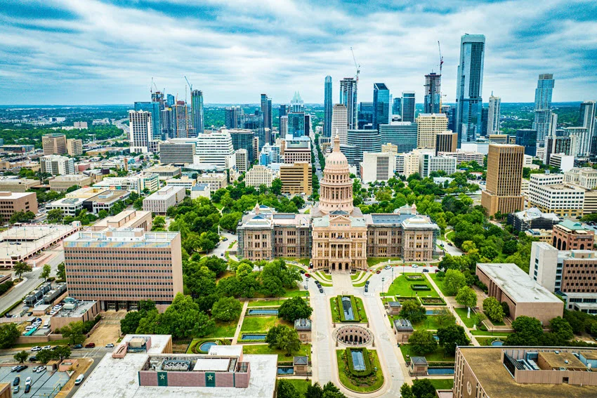 City view of the Texas State Capitol in Austin, with the dome centered above tree-lined grounds and surrounding downtown buildings.