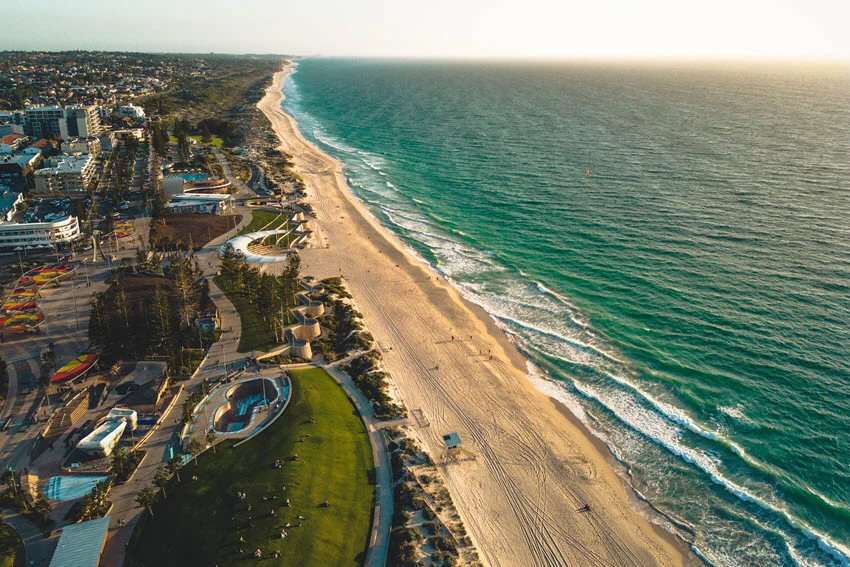 Aerial view of turquoise coastline near Perth, Australia, with a long sandy beach, dunes, and clear water along the shore break.