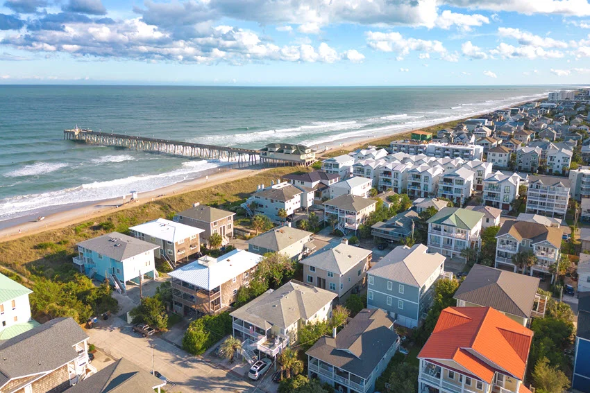 Aerial view of Wrightsville Beach, North Carolina, showing a long pier, coastal homes, and a wide sandy shoreline beside blue water.