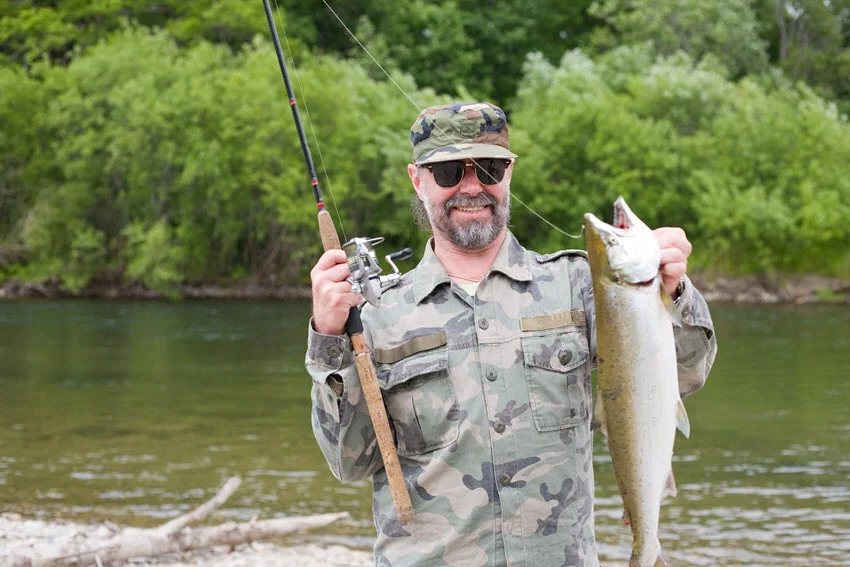 Angler standing mid river holding a landed Salmon, showing wading conditions and the type of water where runs often travel.
