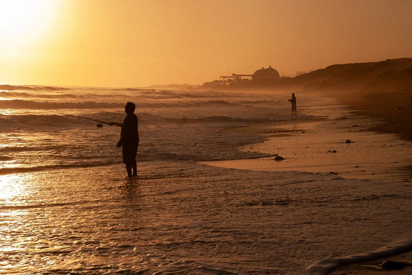 Shore angler casting into the surf at sunset, illustrating land-based Shark fishing from an open beach during low-light conditions.