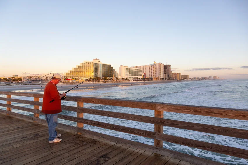 Angler fishing from Daytona Beach Pier at sunrise, showing a classic Florida surf and pier fishing setting for coastal species like Sheepshead.