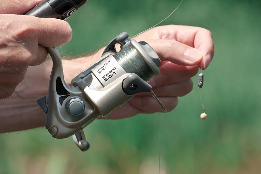 Close-up shot of fishing rod held by an angler, with a visible bread ball hanging from a hook.