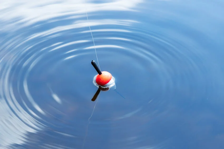 An aerial view of a red topwater lure resting on the surface of the ocean, with gentle ripples surrounding it.