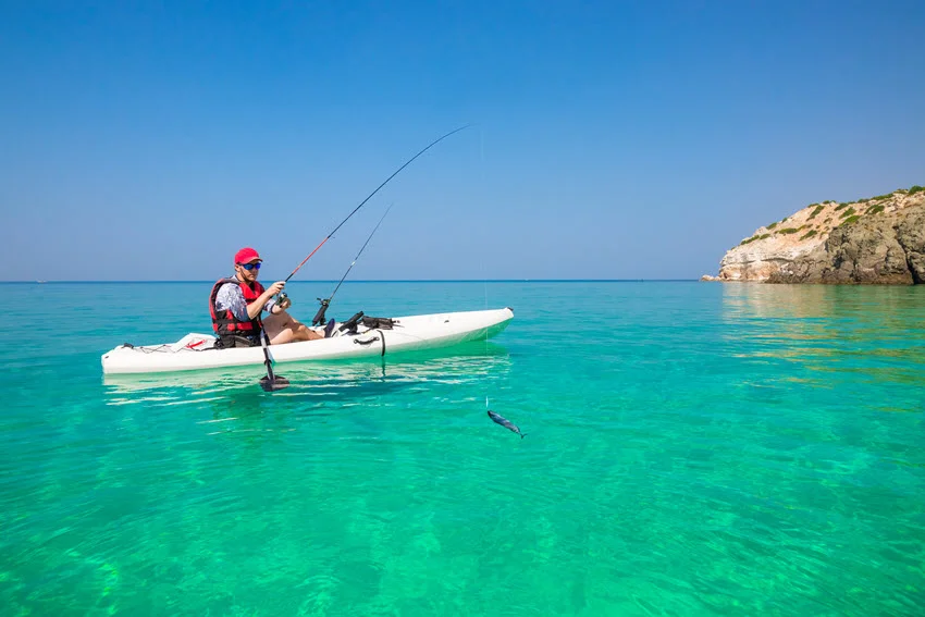 The young angler sits in the white kayak and fishes in the pristine, azure sea water, sight fishing.