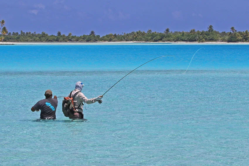 Two anglers wade fishing on shallow tropical flats, casting across clear water and subtle depth changes where fish often patrol along edges, potholes, and tide-driven lanes.
