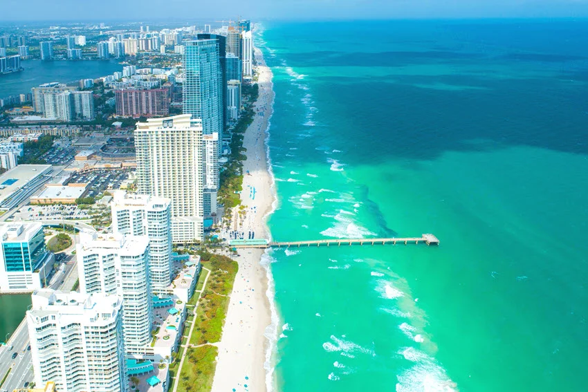 Aerial view of Sunny Isles Beach, Florida, with turquoise water, a long shoreline, and high-rise buildings.