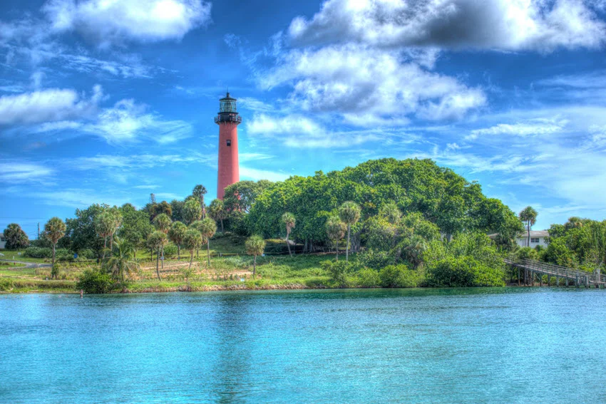 Coastal view of a Florida lighthouse by calm inlet water and greenery, a scenic landmark near fishing areas.