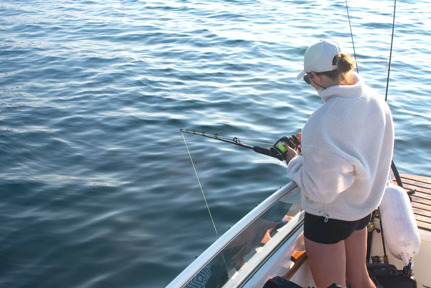 Angler working a jig from a boat's side, focused on the line while drifting over open water.