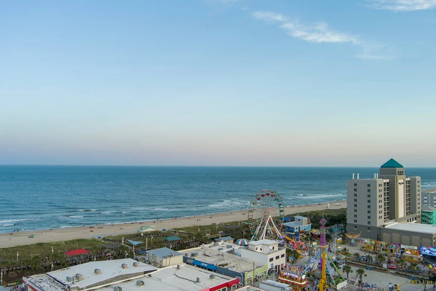 Aerial view of Carolina Beach, North Carolina, showing the boardwalk area, shoreline, and beachfront buildings under clear skies.