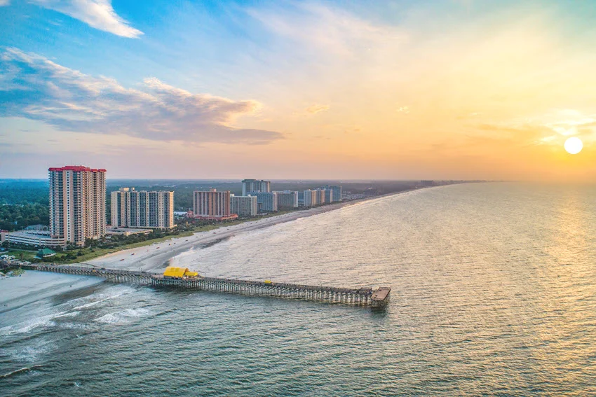 Sunrise view of Myrtle Beach, South Carolina, with a long pier extending into the water and soft light over the shoreline.