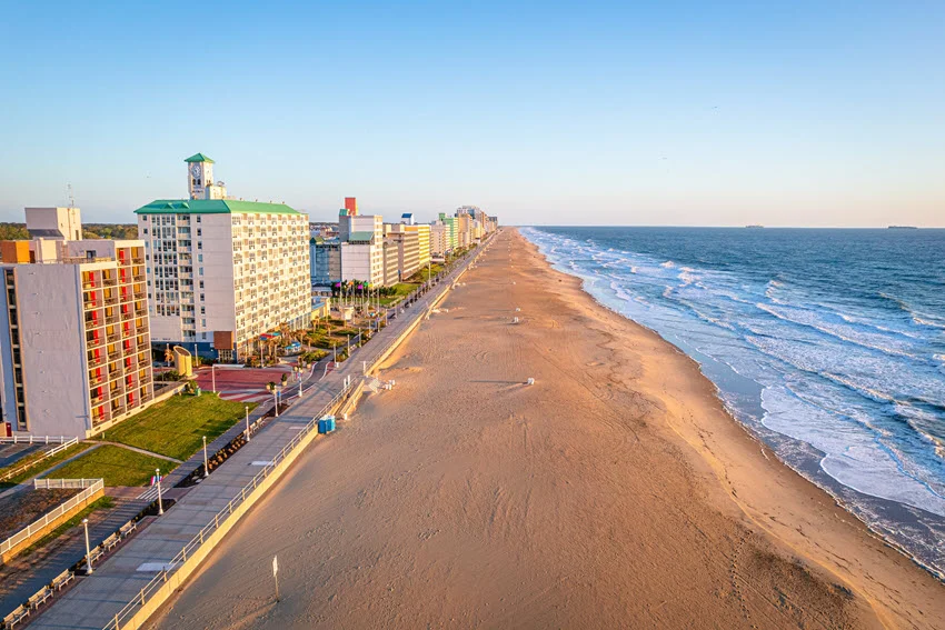 Aerial view of a wide sandy beach in Virginia, with ocean surf, beachfront hotels, and a long stretch of shoreline into the distance.