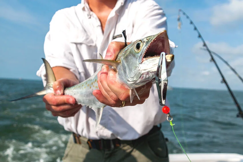 Angler holding a Spanish Mackerel with a metal lure on a boat in Florida saltwater, showing a common setup used for casting and trolling during peak season.